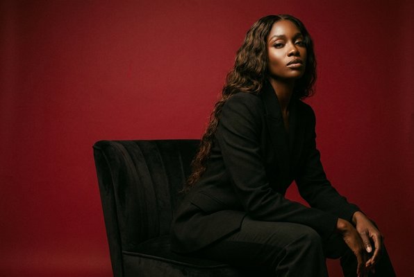 Amara Reign — editorial portrait in black blazer against crimson backdrop