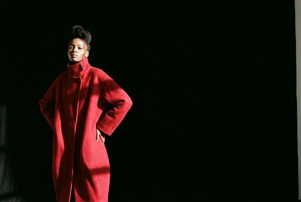 Amara Reign — full-body portrait in crimson red coat against black